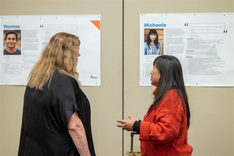 Two women talking to each other while looking at a bulletin board.