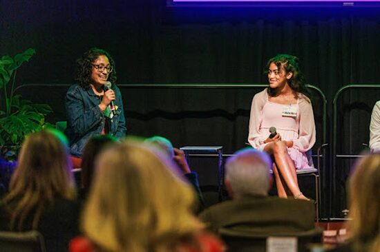Two people speaking on stage with microphones during an event
