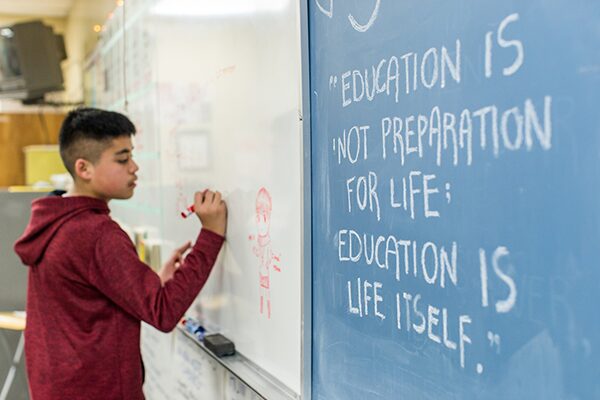 A student at a blackboard which reads "Education is not preparation for life; education is life itself."